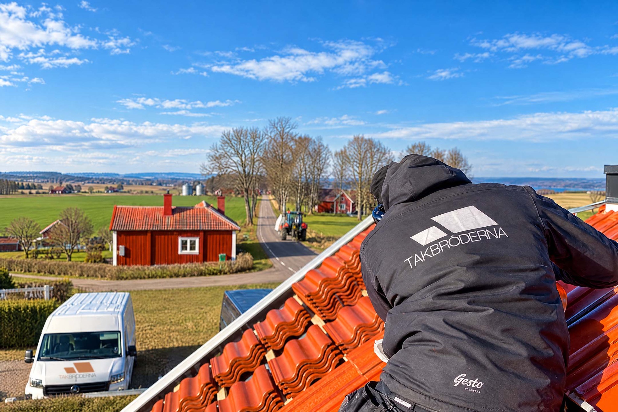 En takläggare från Takbröderna arbetar på ett orange tegeltak med utsikt över landsbygden.